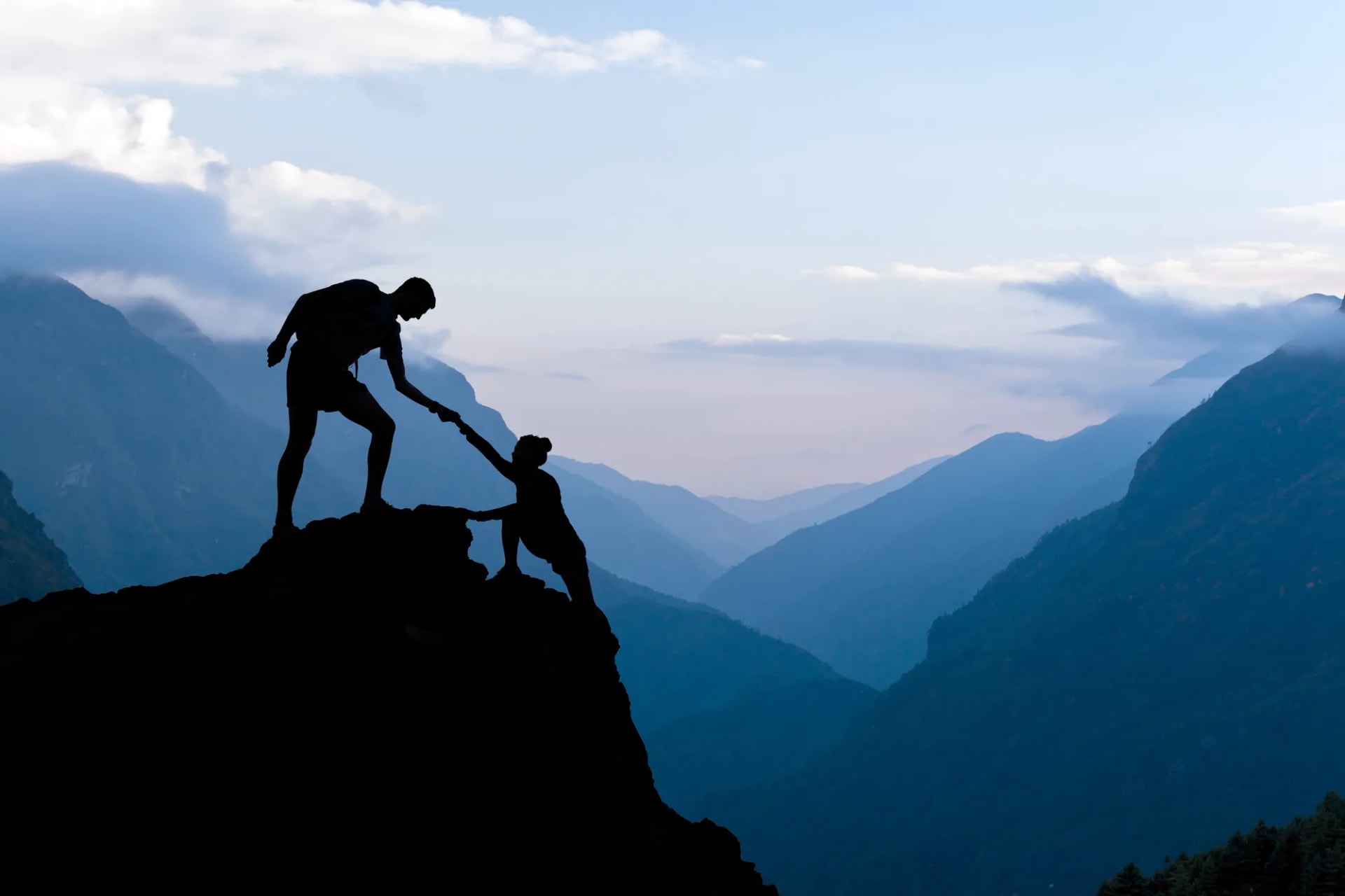 Hikers helping each other on a mountain at sunset