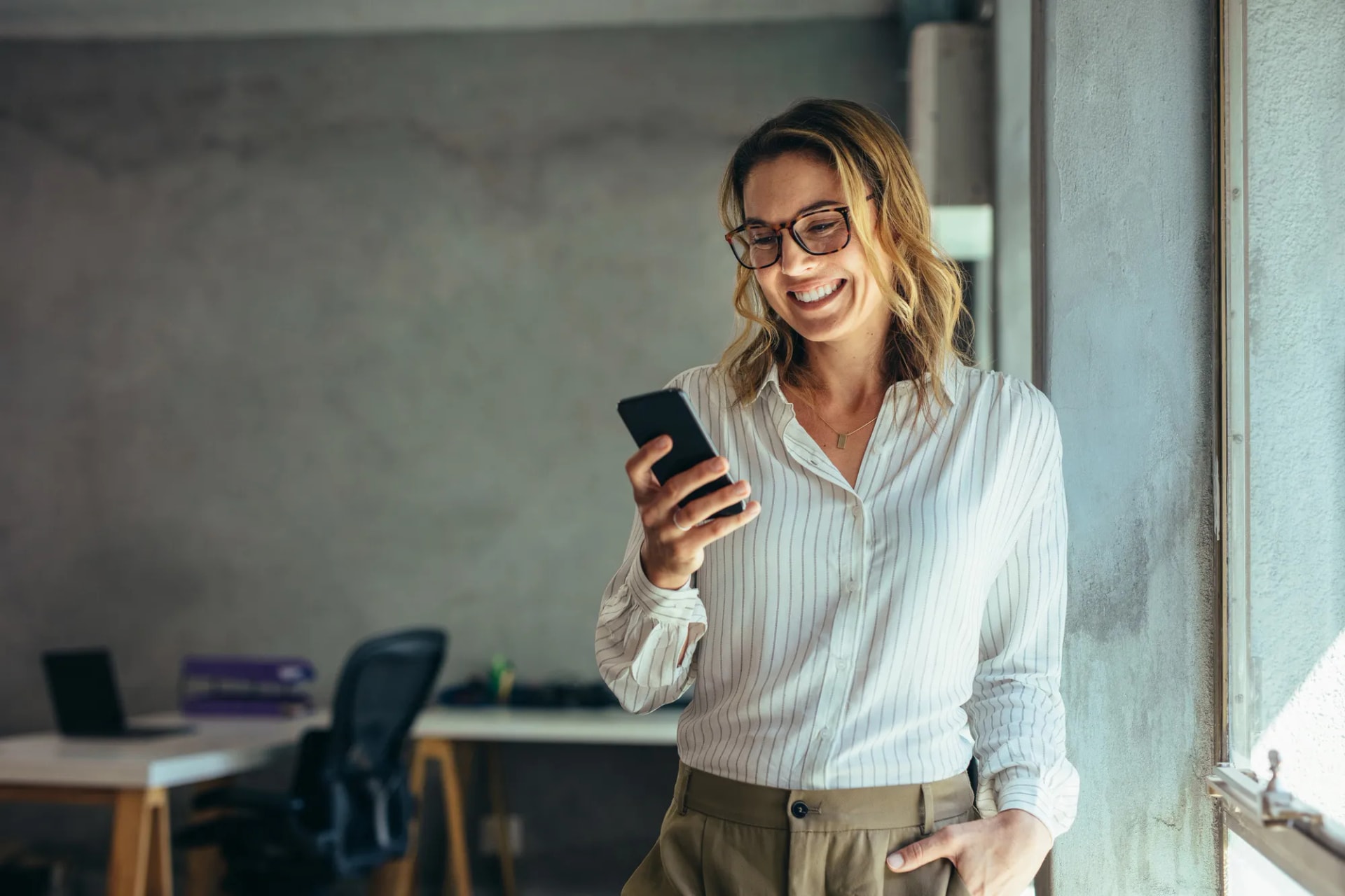 Smiling person checking a phone near an office window